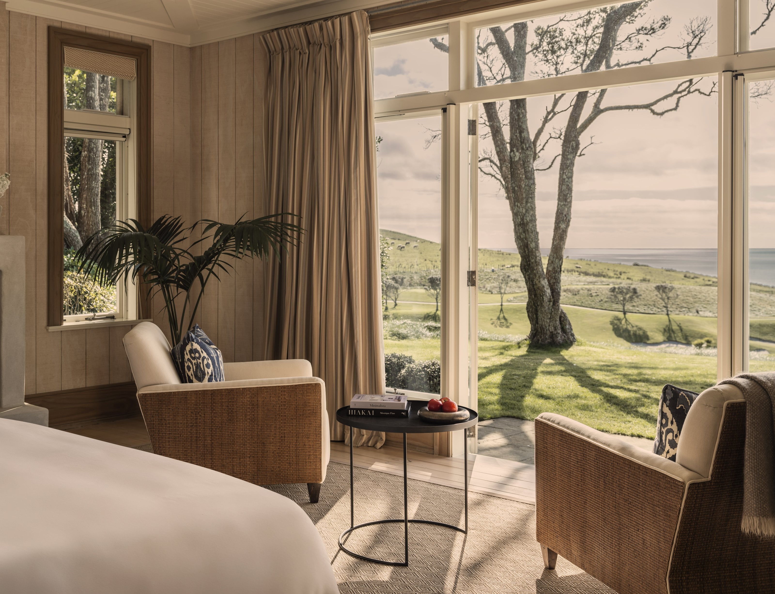 A suite at Kauri Cliffs, two armchairs by open doors onto lawn, farmland and the sea