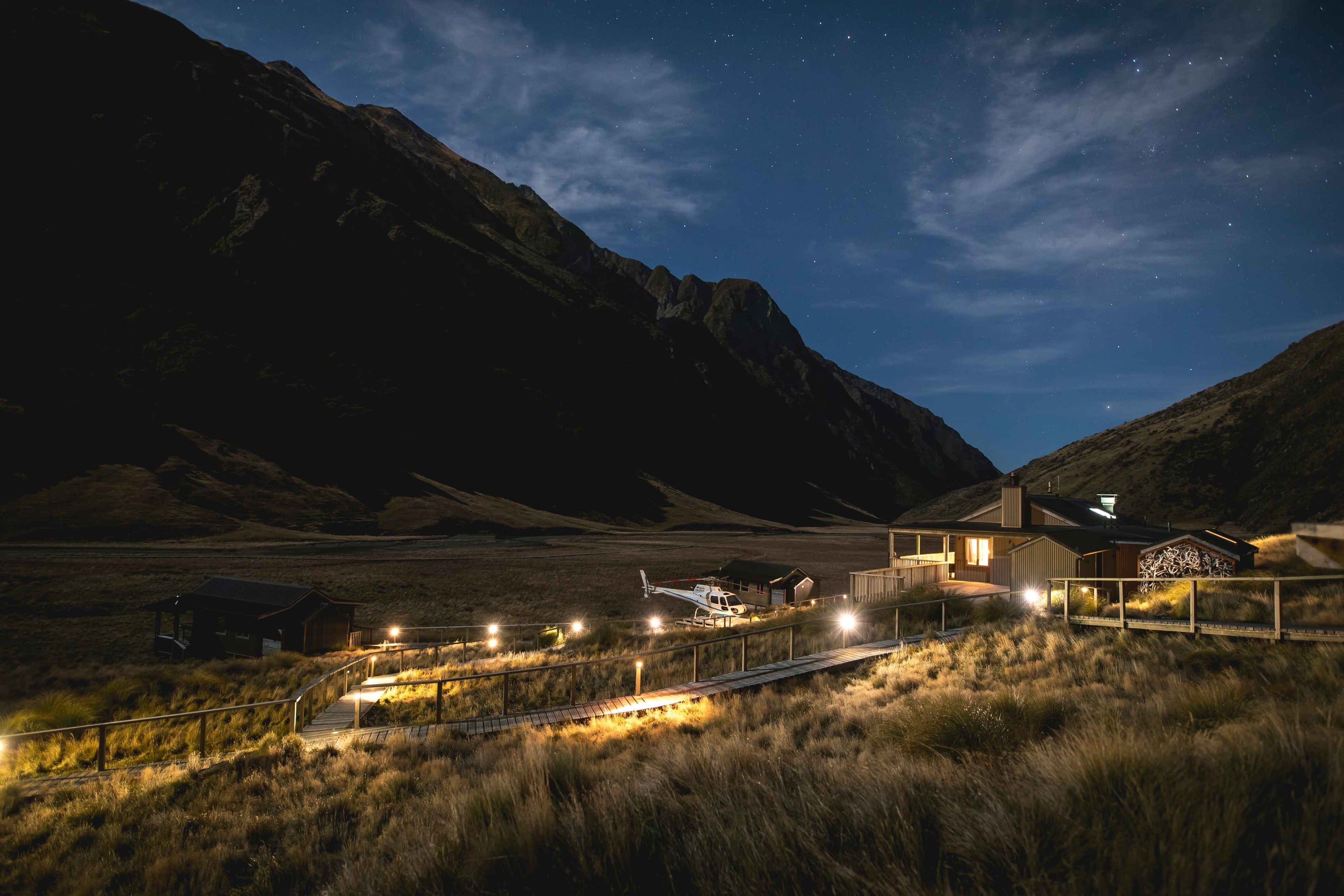 Minaret Station at night, the lit boardwalk and lodge in the valley, a helicopter parked on the flat