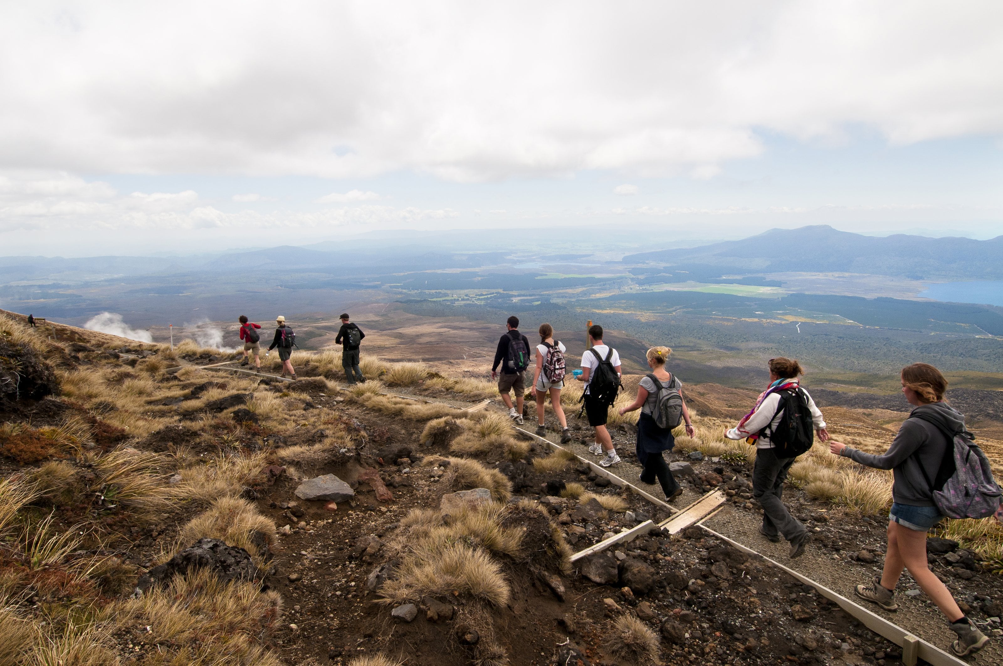 Walkers on a boardwalk high on a volcanic slope, the plains and a lake far below