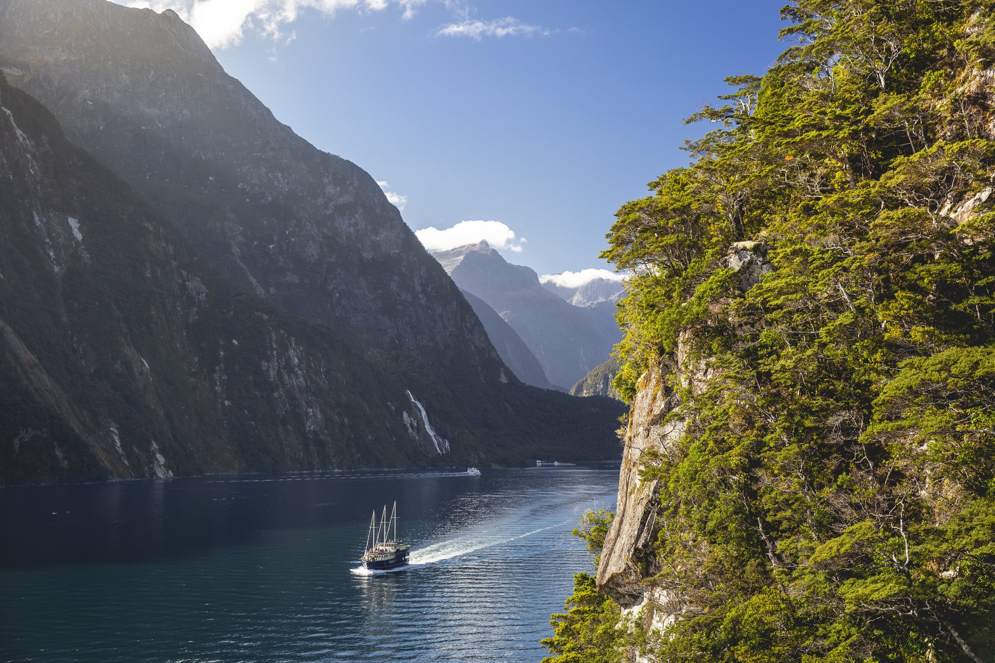 A boat under sail on Milford Sound, a waterfall on the cliff behind
