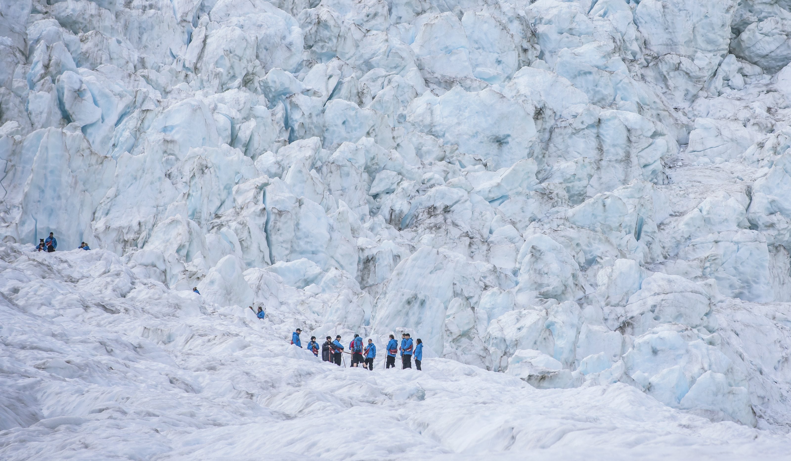 Guided walkers on the ice below the icefall of a West Coast glacier