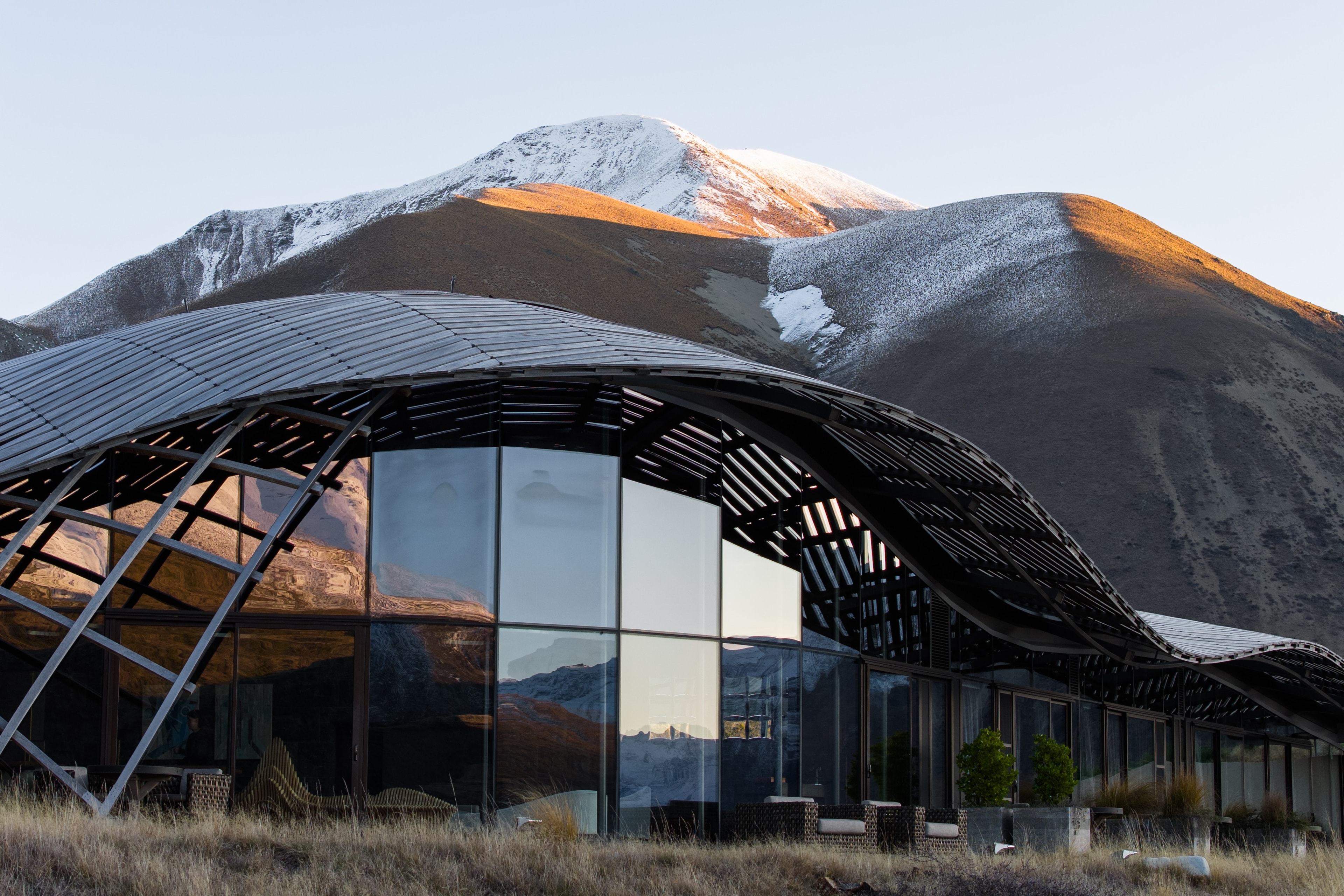 The Lindis lodge, lattice roof and glass facade beneath a snow-dusted peak