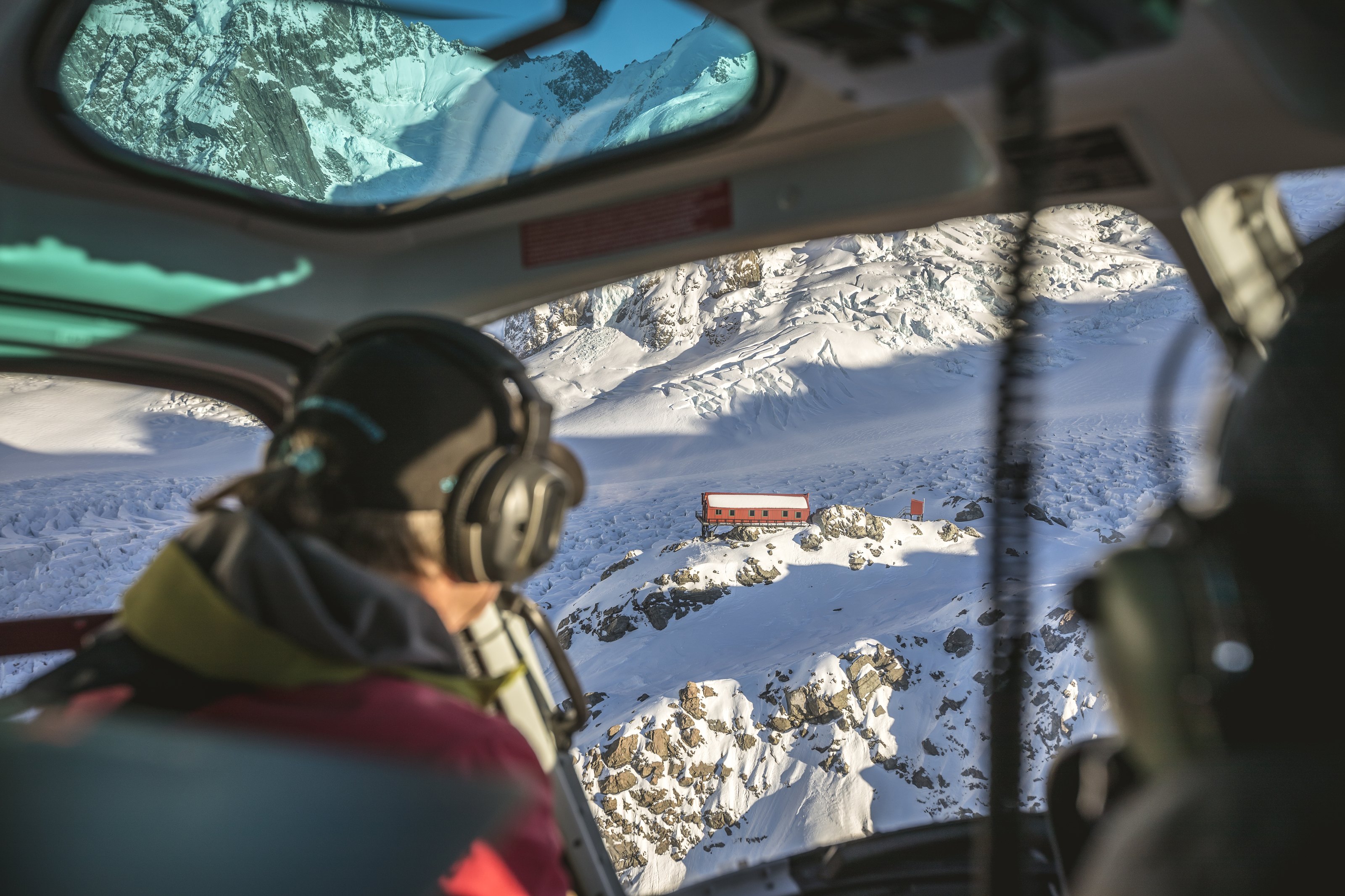 From the helicopter, a pilot looking down on a red mountain hut on the glacier, Southern Alps