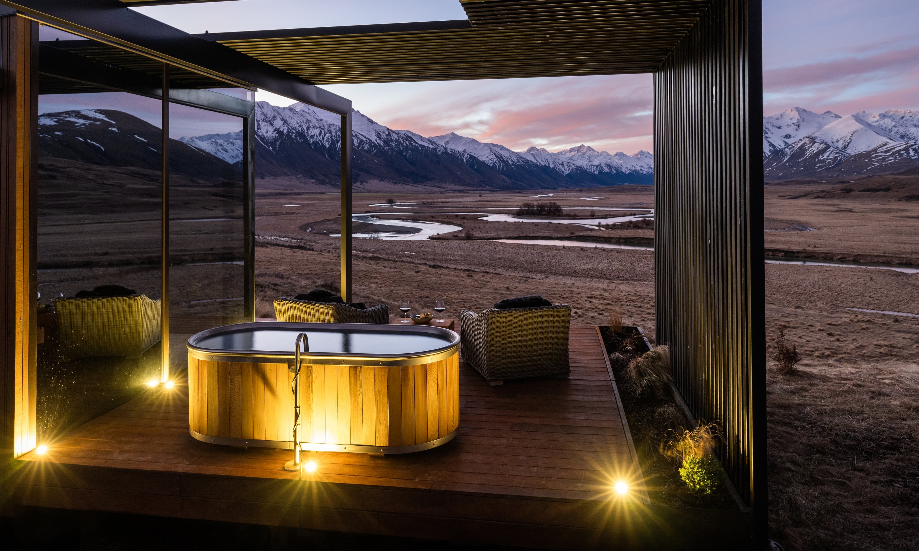 A wooden bath on a deck at The Lindis at dusk, the Ahuriri valley and snow-capped mountains beyond