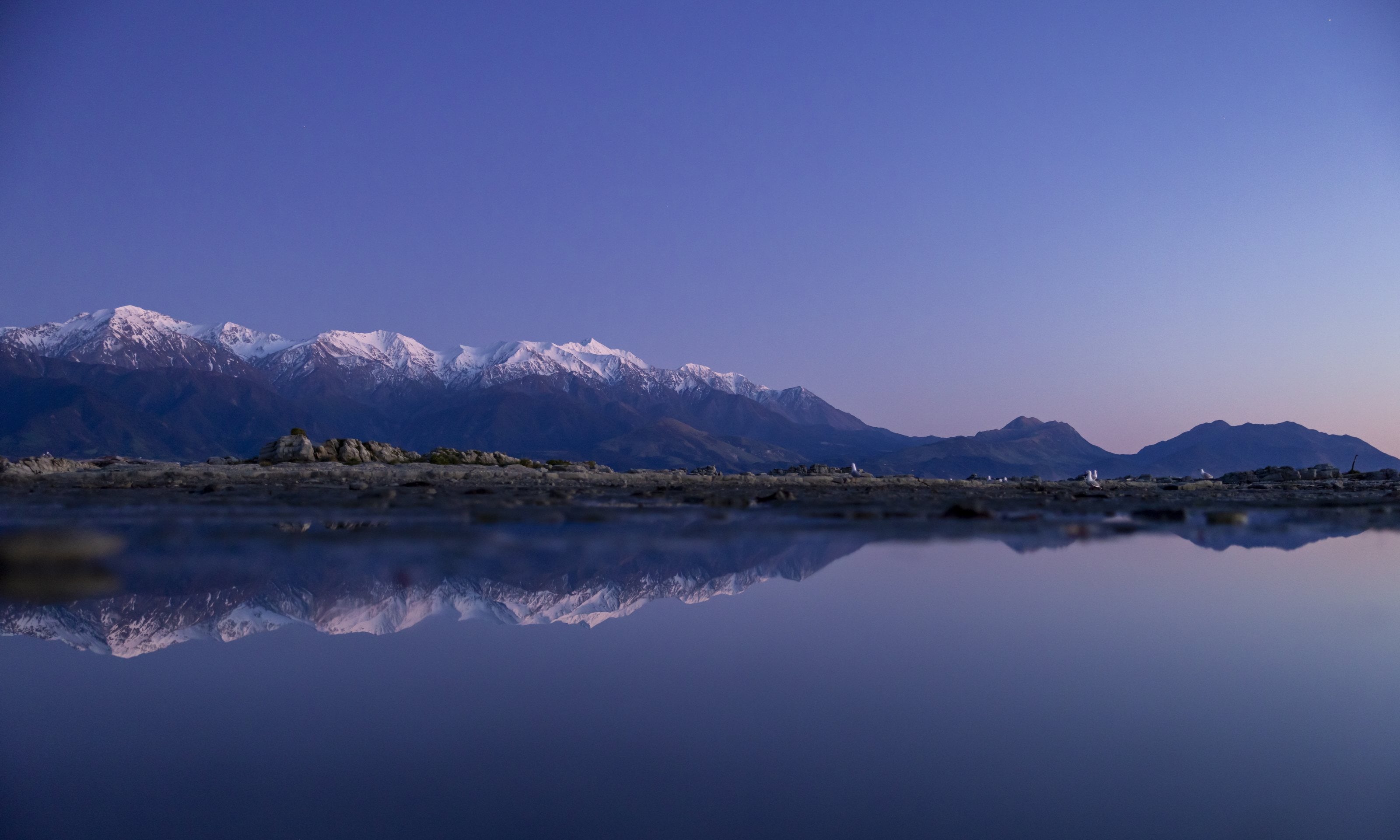 The Seaward Kaikōura Range under snow at dusk, mirrored in still water along the shore