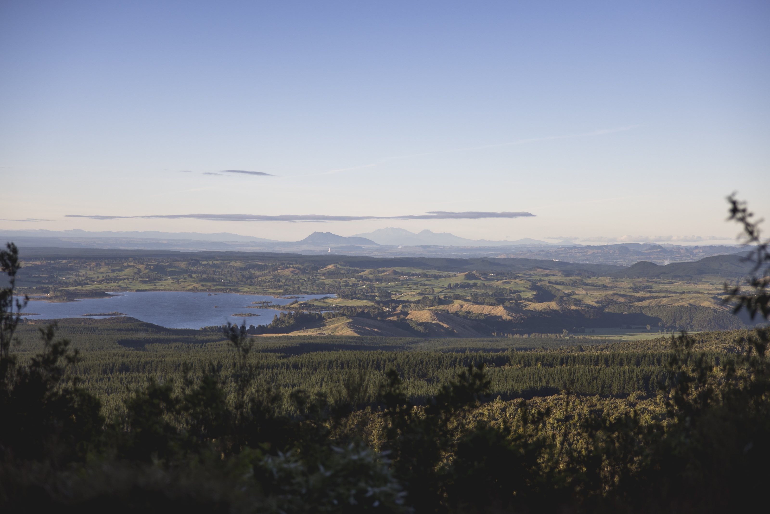 A lake among farmland and pine forest, the volcanoes of the Central Plateau on the horizon