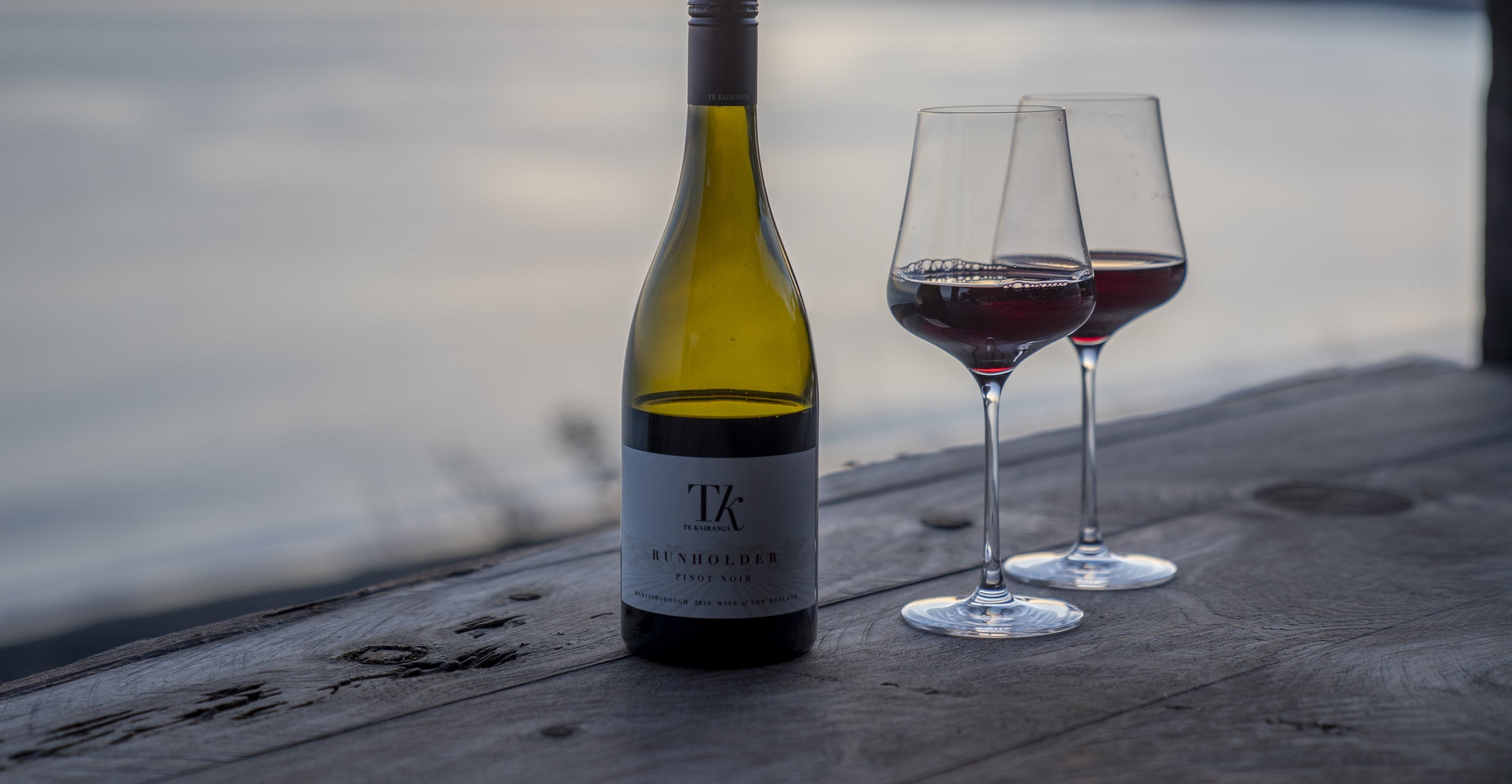 A bottle of Martinborough pinot noir and two glasses on a weathered table at dusk